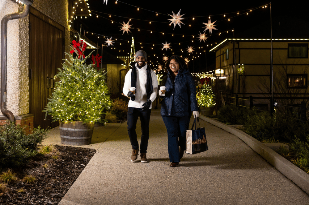 Two people walking through Antler Village at Biltmore at nigth during the holidays