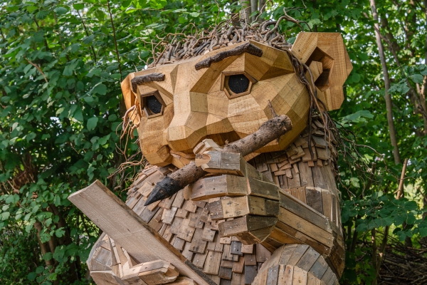 A troll by Thomas Dambo made from reclaimed wood, writing with a wood pencil on a piece of wood.