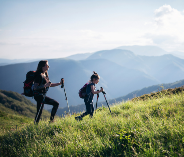 Two women with walking sticks are hiking a mountaintop